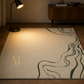 A large area rug in a warm cream color with a dark green wavy line pattern and a gold monogram logo, styled on a wooden floor in a modern room with a lamp and cabinet.