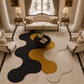A modern abstract wavy area rug in black, mustard yellow, and cream, styled in a luxurious, symmetrical living room with classic cream-colored armchairs, a matching sofa, and elegant side tables.