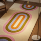 Colorful geometric-patterned rug on a wooden floor with a chair and lamp in the background.