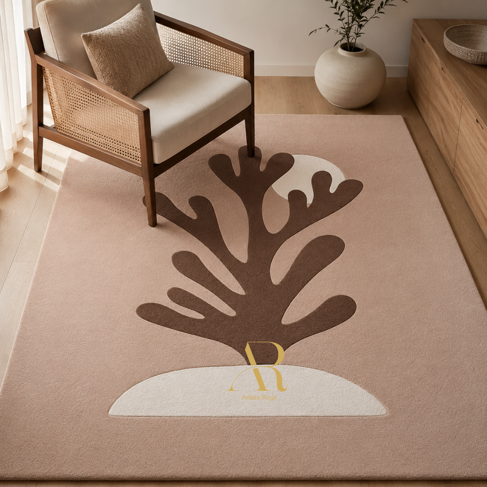 A rectangular area rug in a warm beige tone with a large stylized brown coral or tree-like motif and a white crescent shape, styled in a bright living room beside a wooden armchair and vase.