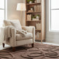 Beige armchair with a blanket in a room with a wooden bookshelf and patterned rug.