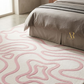 Bedroom with a patterned pink and white rug and beige bedding.