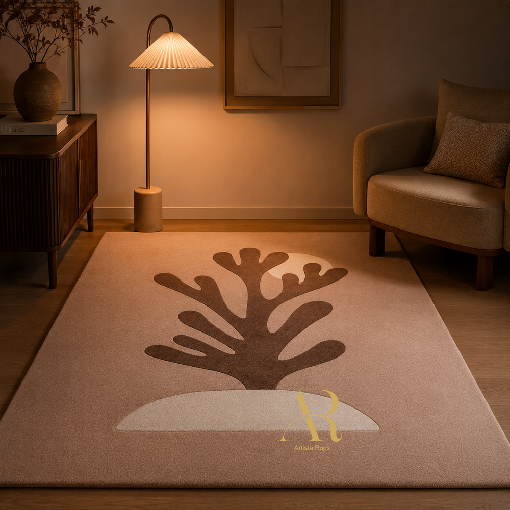 A rectangular area rug in a warm beige tone with a large dark brown coral-like motif and a white curved shape near the bottom, styled in a cozy living room with a floor lamp, armchair, and wooden cabinet.