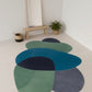 Colorful rug on a light wooden floor with a mirror and plant in the background.