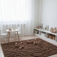Children's playroom with a brown textured rug, white furniture, and toys.