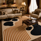 A large area rug with a cream base, orange stripes, and black organic shapes, styled in a luxurious, ornate living room with a sofa, armchair, and wooden coffee table.