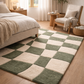 Checkered green and beige rug in a bedroom with a bed and chair.