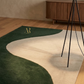 Two area rugs with a wavy design on a wooden floor, one green and one beige, with a wooden cabinet in the background.
