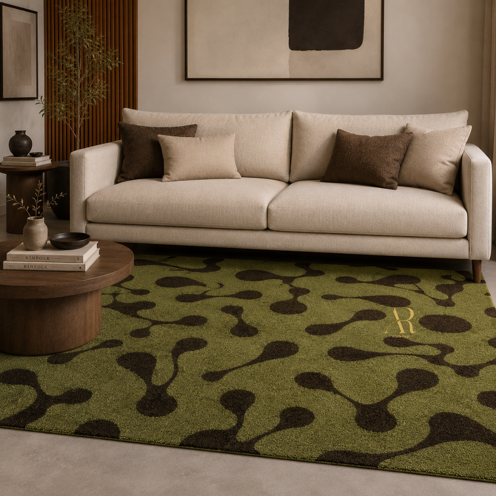 A green area rug with a dark brown abstract organic pattern and a gold monogram letter 'R', styled in a modern living room setting under a cream sofa.