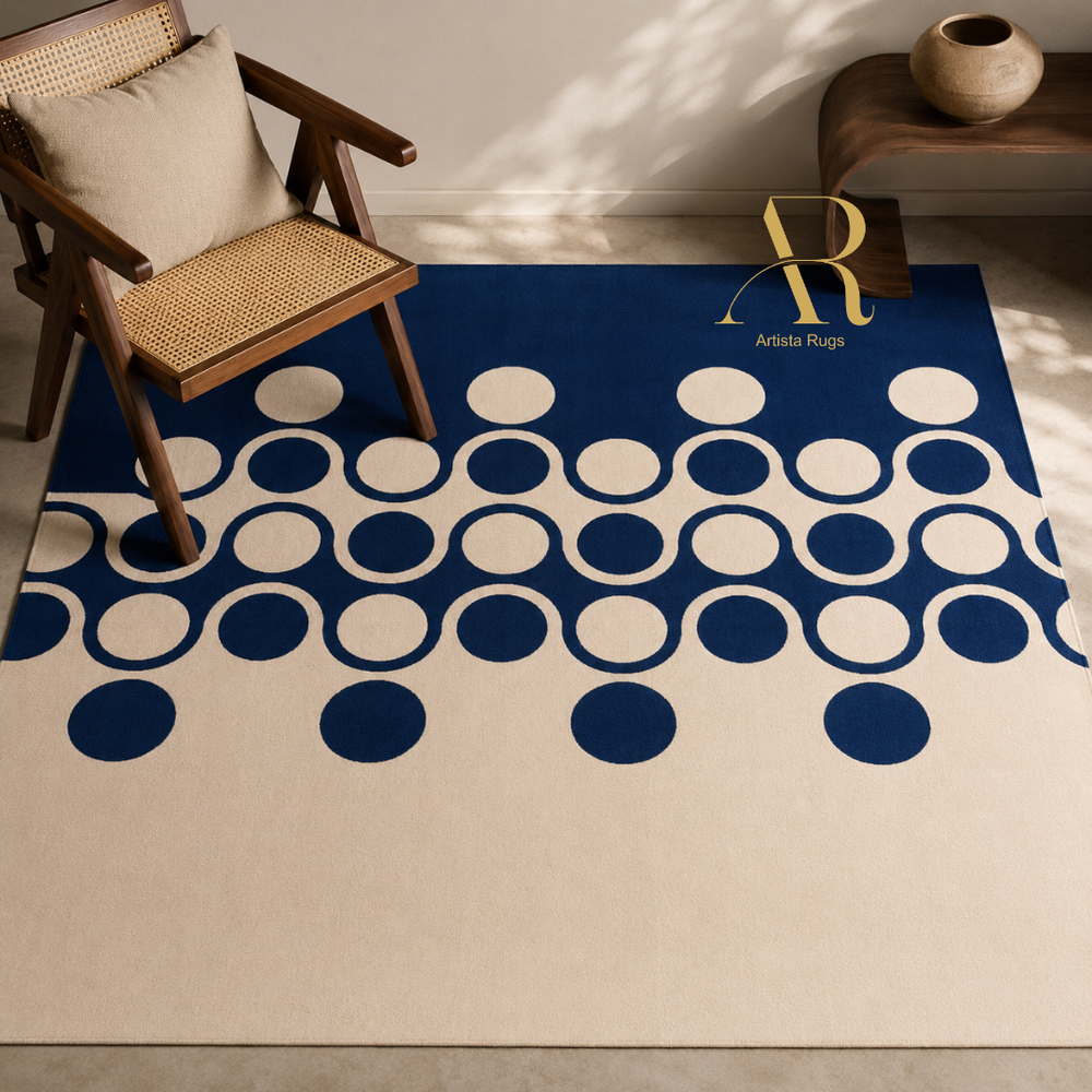 A cream-colored area rug with a bold navy blue geometric pattern of overlapping circles, styled in a modern room setting with a wooden armchair and a side table.