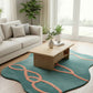 Living room with a teal rug featuring pink patterns, a beige sofa, wooden coffee table, and plants.