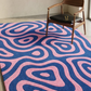 Pink and blue patterned rug with a wooden chair and black cushion.