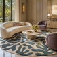 A luxury modern living room featuring a large curved cream sofa, a round marble coffee table, a plush purple armchair, and a large circular area rug with an abstract blue-gray and beige pattern.