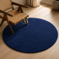 A round navy blue area rug on a light wood floor, styled with a wooden cane-back chair and a curtain in the background.