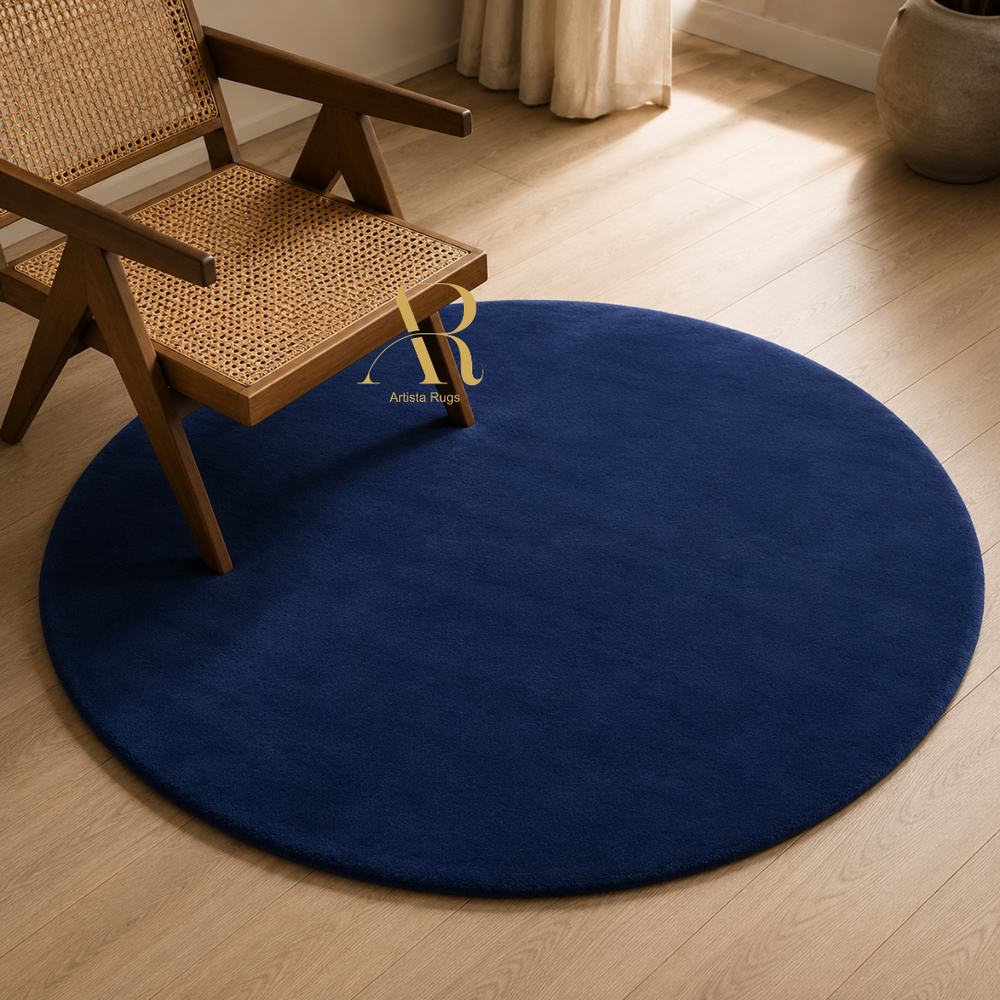 A round navy blue area rug on a light wood floor, styled with a wooden cane-back chair and a curtain in the background.