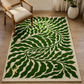 A rectangular area rug with a bold green leaf pattern on a cream background, styled in a living room setting next to a wooden armchair.