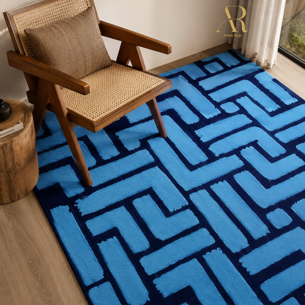 A blue and navy geometric patterned area rug styled in a modern living room setting next to a wooden armchair and a side table.