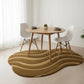 Dining table with chairs on a wavy rug in a minimalistic room.