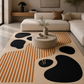 A modern area rug with an abstract design featuring black organic shapes, orange stripes, and a beige base, styled in a contemporary living room setting.