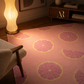 A pink area rug with a repeating pattern of pink grapefruit slices, styled in a warm, modern living room setting next to a glowing wavy floor lamp and a mid-century modern chair.