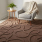 Gray armchair with a blanket on a patterned brown rug in a room with a small table and plant.