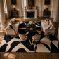 A luxury living room featuring a large black and cream abstract patterned area rug by Artoise Rouge, styled with two cream sofas, two matching armchairs, and a dark wood coffee table.