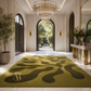 A large rectangular area rug with an abstract wavy pattern in olive green and dark brown, displayed in a luxurious white entryway with marble floors, a gold chandelier, and potted plants.