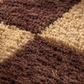 Close-up of a shaggy area rug with a geometric patchwork pattern in dark brown, medium brown, and warm beige, showing the textured pile detail.
