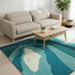 Living room with a beige sofa, wooden coffee table, and a blue abstract rug.