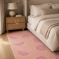 A pink area rug with a repeating citrus slice pattern, styled in a bedroom next to a bed with beige linens and a wooden nightstand.