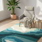 Living room with a blue and green abstract rug, gray armchair, and potted plant.