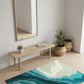 Modern interior with a wooden bench, mirror, and abstract rug on a light wood floor.