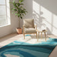Modern room with a blue and green abstract rug, beige armchair, and potted plant.