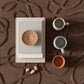 Ceramic items including a bowl, cups, and a book on a textured brown surface.