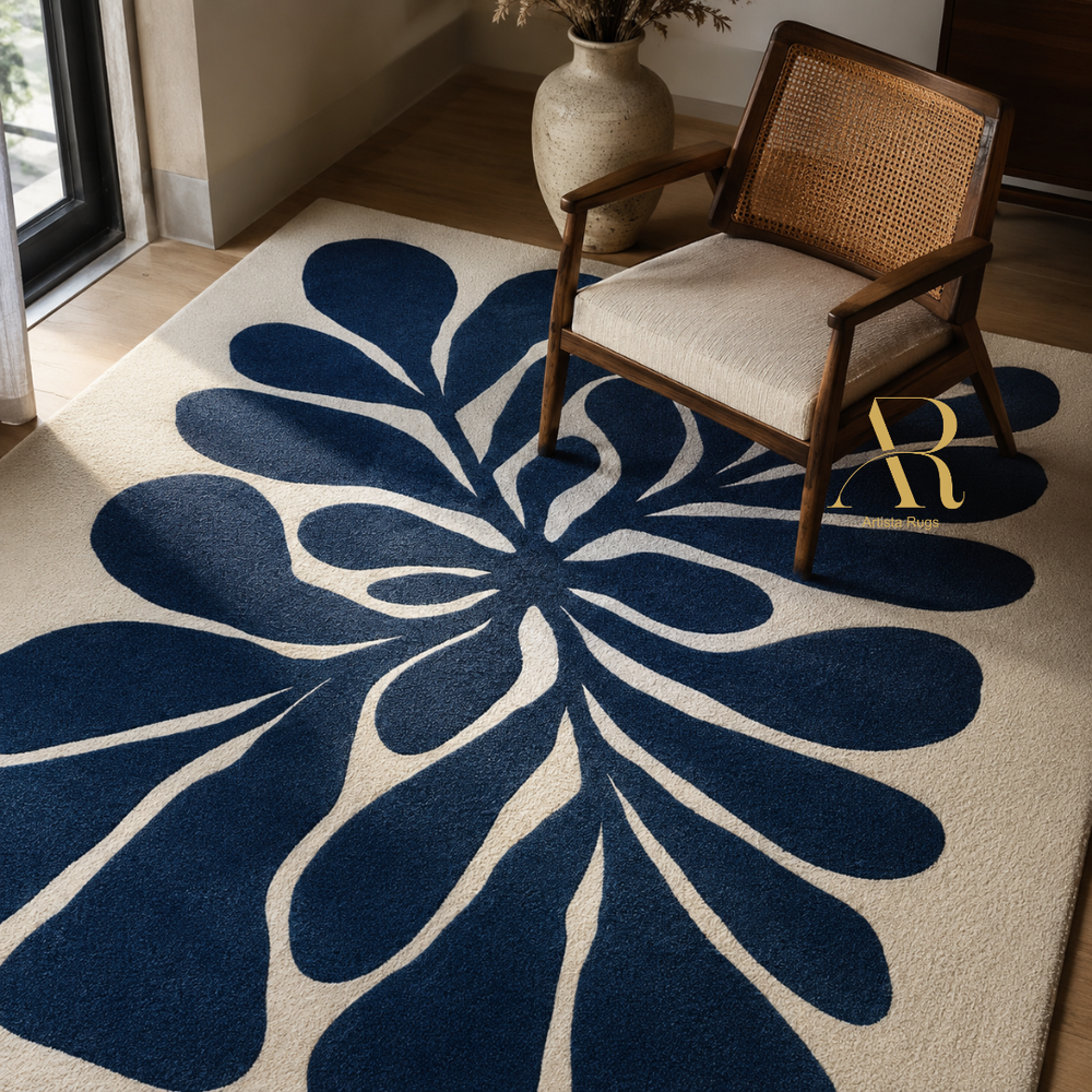 A large area rug with a bold, mid-century modern floral or leafburst pattern in dark navy blue on a warm cream background, styled in a living room next to a wooden armchair.