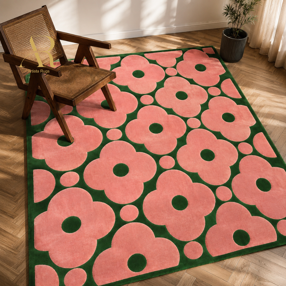 A rectangular area rug with a bold retro floral pattern in pink and dark green, styled on a light wood floor next to a wooden armchair.