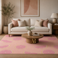 A styled living room scene featuring a pink area rug with a repeating citrus slice pattern, a cream sofa with blush and beige pillows, a round wooden coffee table, and a potted plant in a neutral-toned interior.