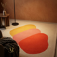 Colorful abstract rug on a beige floor with a brown wall and wooden side table.