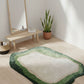 Green and beige rug on a wooden floor with a mirror and plant in the background.