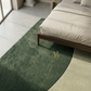 Green rug with gold logo on a bedroom floor next to a bed