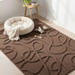Brown patterned rug with a white pet bed and toys in a room with a small table and plant.