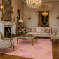 A pink area rug with a large pink and yellow citrus slice pattern is styled in an ornate, classic European living room with gold accents, a marble coffee table, and floral armchairs.