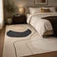 A modern abstract area rug in a styled bedroom setting, featuring organic shapes in cream, beige, and charcoal gray with black line details, shown on a wooden floor next to a bed.