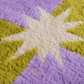 Close-up of a plush, high-pile rug featuring a starburst pattern in cream, lavender purple, and olive green.