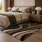 A modern area rug with an abstract wavy pattern in beige, brown, black, and cream, styled on a light wood floor in a contemporary bedroom setting.