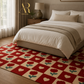 A red and beige checkered area rug with a repeating heart and tulip pattern, styled in a cozy bedroom setting under a bed with neutral bedding.