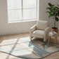 Beige armchair in a room with a large window, rug, and plant.