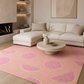 A pink area rug with a repeating pink grapefruit slice pattern is styled in a modern living room setting with a cream sectional sofa and a round wooden coffee table.