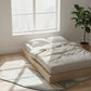 Minimalist bedroom with a wooden platform bed, white bedding, and a plant.