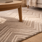 Close-up of a textured rug with geometric pattern on a wooden floor, partially covered by a wooden coffee table.